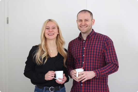 Two Userlike support members, smiling at the camera, holding coffee cups.